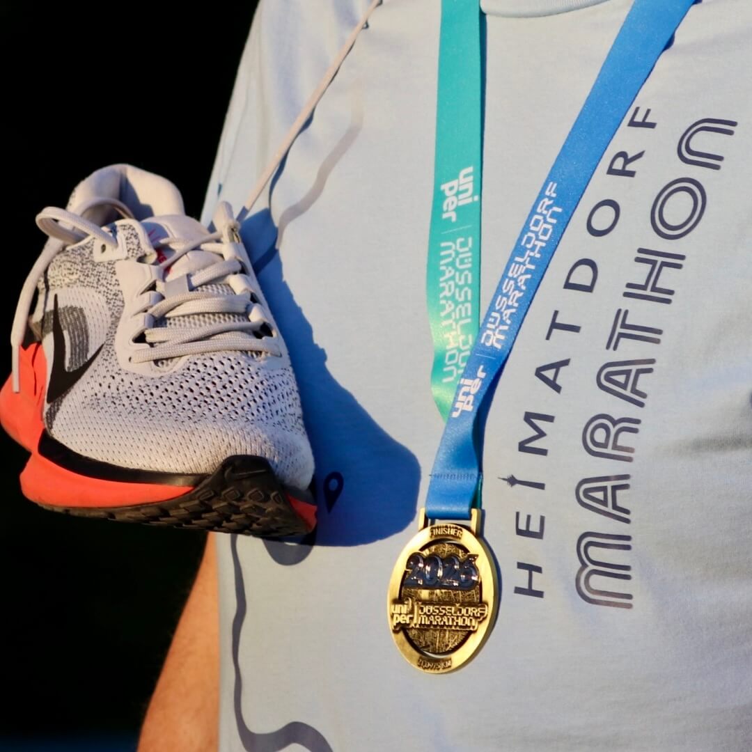 Ein Mann hat das Düsseldorf HEIMATDORF Marathon T-Shirt an und eine Medaille um den Hals