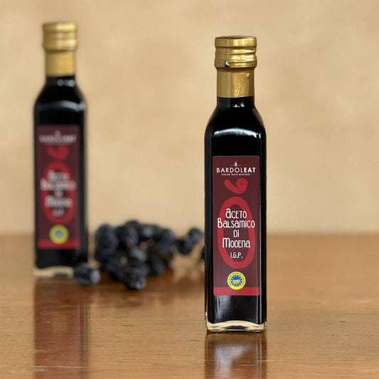Flasche Aceto Balsamico di Modena steht auf einem Tisch mit Weintrauben im Hintergrund.