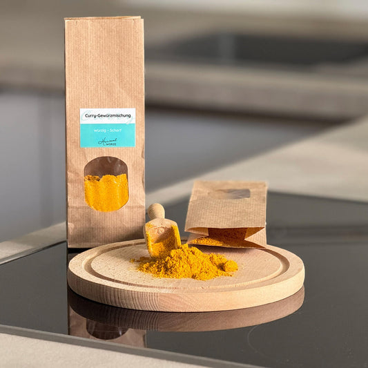 Tütchen mit Curry-Gewürzmischung steht in einer Küche. Davor ist auf einem Holzbrett etwas Curry-Pulver ausgeschüttet.