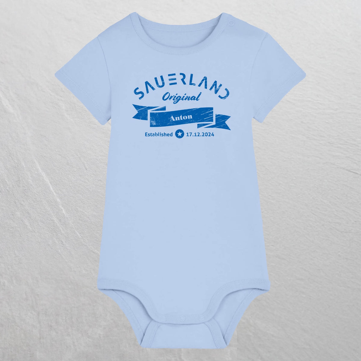 Hellblauer Baby-Body mit dunkelblauem Aufdruck Sauerland Original, dem Vornamen und Geburtsdatum des Babys.