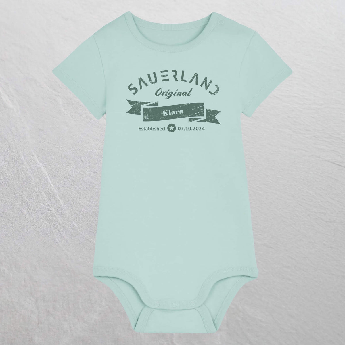 Karibikblau farbiger Baby-Body mit dunkelgruenem Aufdruck Sauerland Original, dem Vornamen und Geburtsdatum des Babys.