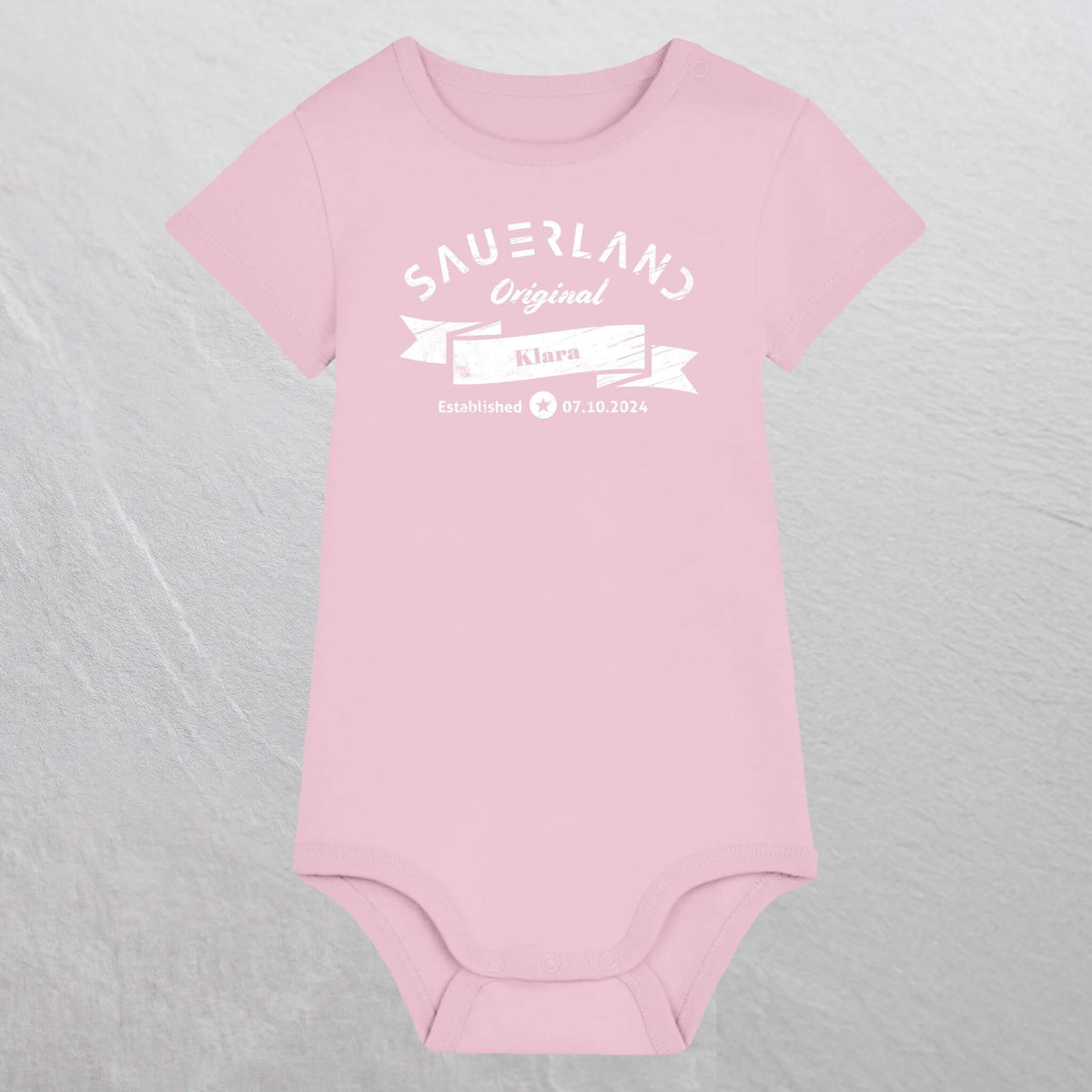 Rosa farbiger Baby-Body mit weißem Aufdruck Sauerland Original, dem Vornamen und Geburtsdatum des Babys.
