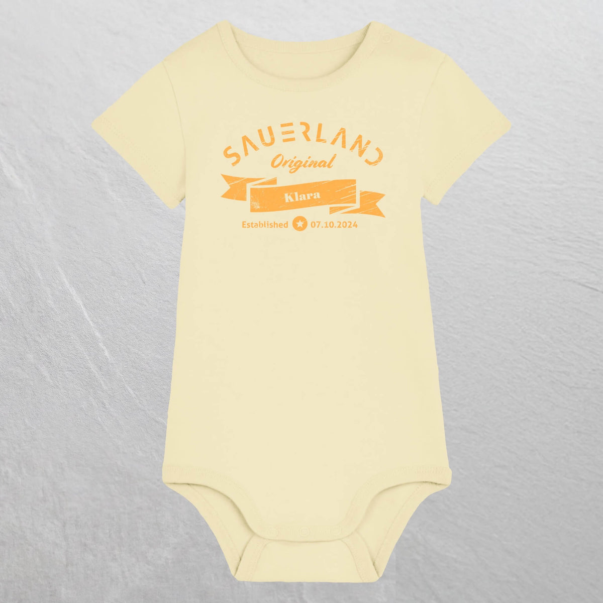Zartgelber Baby-Body mit gelbem Aufdruck Sauerland Original, dem Vornamen und Geburtsdatum des Babys.