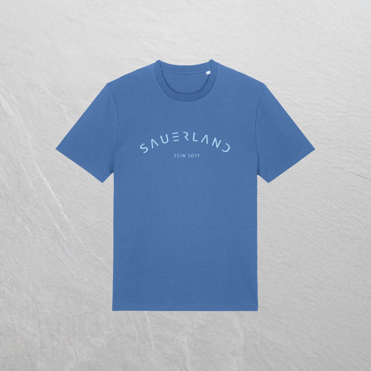 Mittelblaues T-Shirt mit leicht gerundetem Sauerland-Schriftzug liegt auf einem Holzhintergrund. In der Mitte unter dem Sauerland-Schriftzug ist der Dorfname Kierspe eingedruckt. Der Aufdruck ist hellblau.
