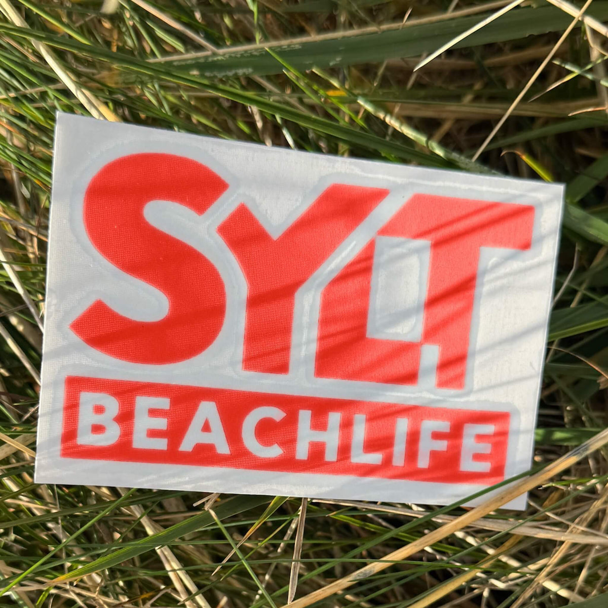 Sylt Aufkleber Beachlife in rot liegt an einem Strand