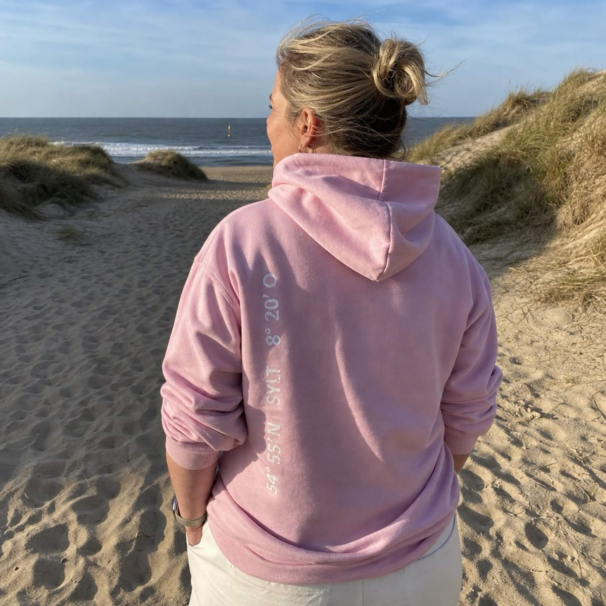 Rosa farbiger Hoodie mit weißem Aufdruck, der senkrecht auf der linken Seite des Rückens verläuft. Aufgedruckt sind die Koordinaten von Sylt.