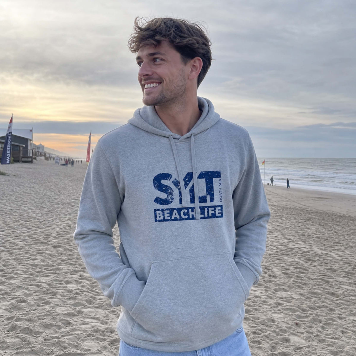 Mann in grauem Hoodie mit dunkellblauen 'SYLT NORTH SEA BEACHLIFE' Logo, steht auf Sylt.