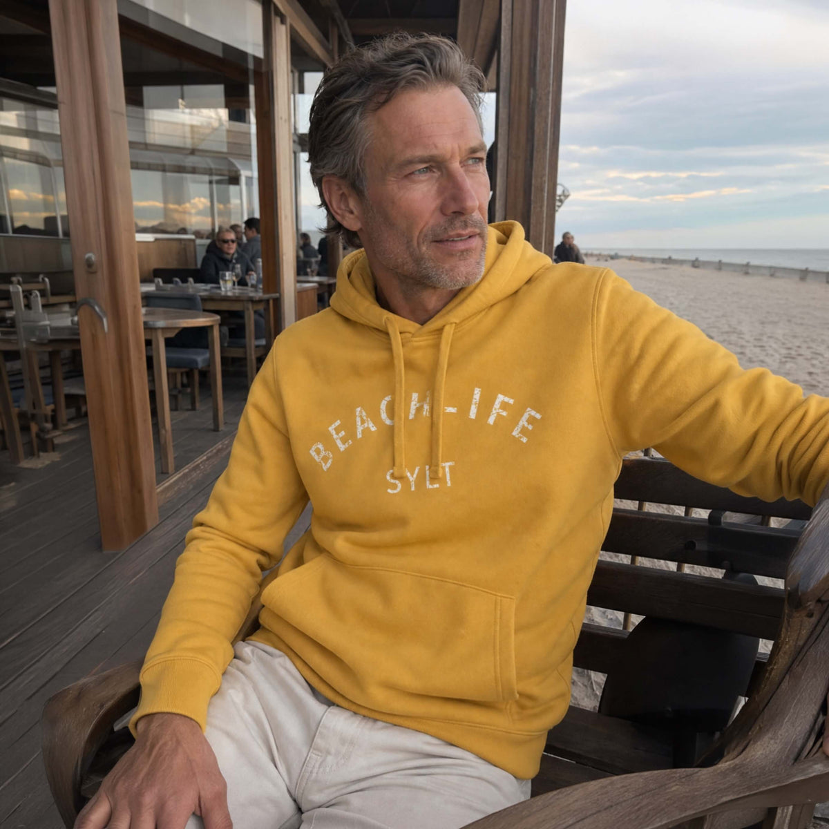 Ein Modell sitzt auf Sylt mit einem gelben Sylt Hoodie