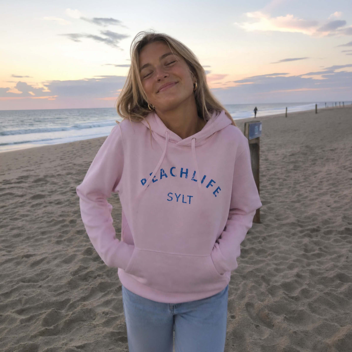 Ein Modell steht am Strand auf Sylt  auf Sylt mit einem pinken Sylt Hoodie