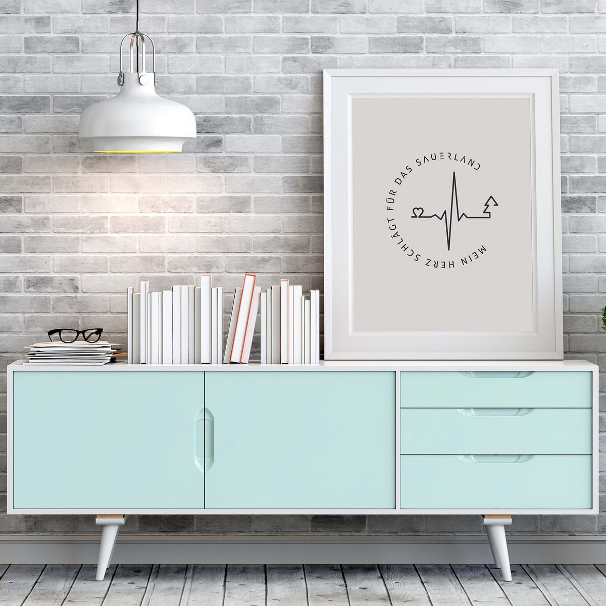 Weißer Bilderrahmen mit hellgrauem Poster mit dunkelgrauen Mein Herz schlägt für das Sauerland-Logo, steht auf einem türkisfarbenem Sideboard.  