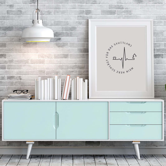 Weißer Bilderrahmen mit hellgrauem Poster mit dunkelgrauen Mein Herz schlägt für das Sauerland-Logo, steht auf einem türkisfarbenem Sideboard.  