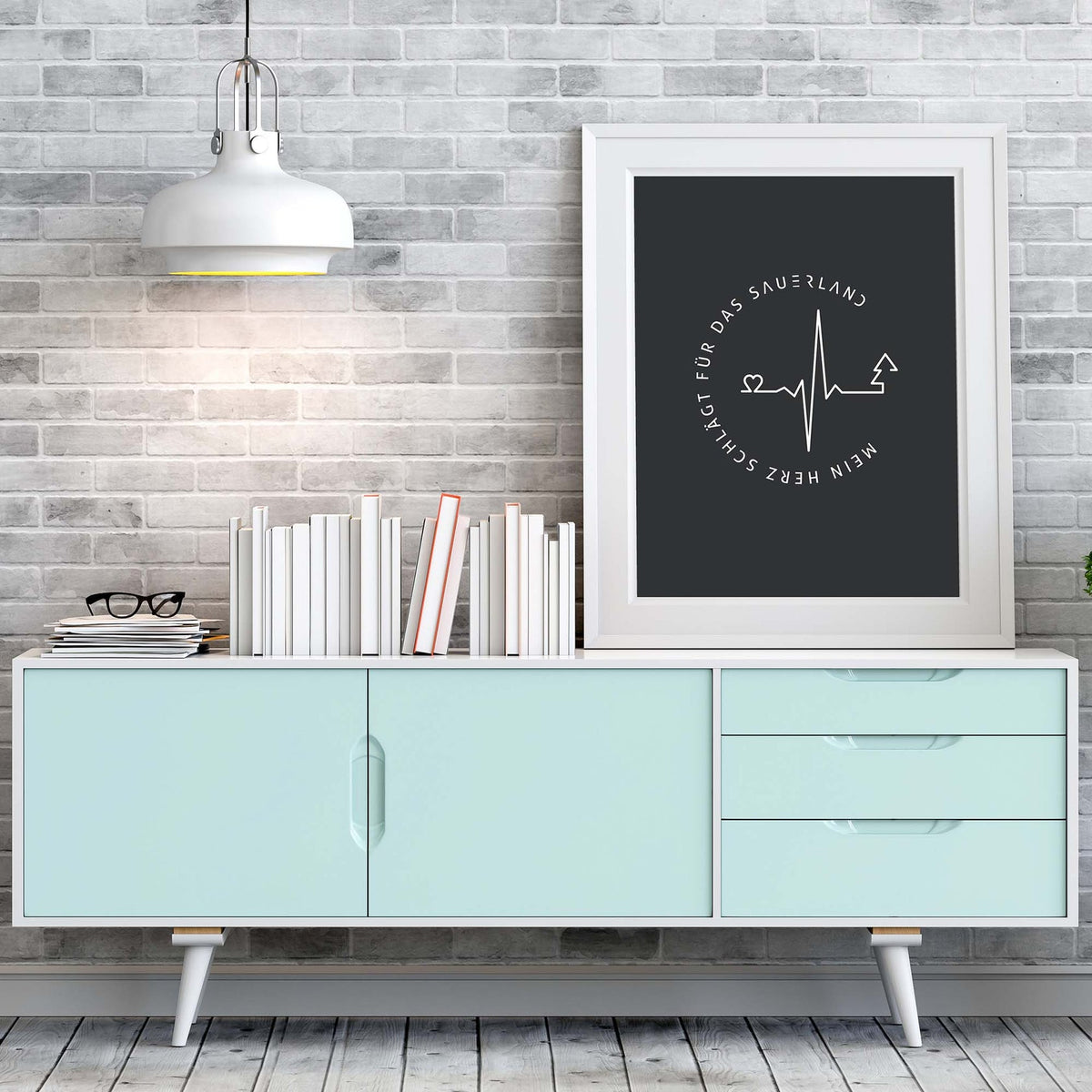 Weißer Bilderrahmen mit anthrazitfarbigem Poster mit weißem Mein Herz schlägt für das Sauerland-Logo, steht auf einem türkisfarbenem Sideboard.